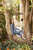 A young woman wearing a blue jacket and jeans sitting in a tree
