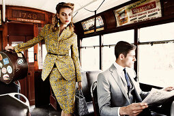 A young woman wearing an elegant suit and a young man wearing a grey blazer on a train