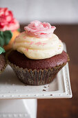 A chocolate cupcake with vanilla cream and a sugar rose