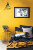 Bett und Nachttisch aus Metall vor gelber Wand