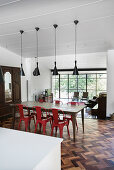 Wooden dining table and red chairs below pendant lamps with view onto terrace in background