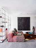 Red designer sofa, coffee table and picture in front of floor-to-ceiling, transparent shelves in open living space
