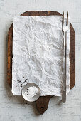 Pergamentpapier auf Holzschneidebrett mit Fleischgabel, Salz und Pfeffer