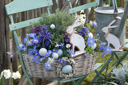 Basket with ray anemones, hyacinths and thyme on chair in the garden