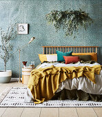 Doppelbett mit Kissen, darüber Zimmerpflanze, Nachttisch, Stehlampe und Olivenbäumchen im Schlafzimmer mit jadegrüner Tapete