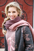 A young blonde woman wearing a scarf and a pink and grey knitted coat