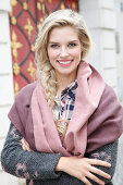 A young blonde woman wearing a shawl and a pink and grey knitted coat