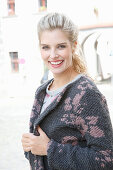 A young blonde woman wearing a pink and grey knitted coat