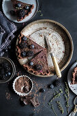 Chocolate tart topped with blackberries and blueberries on a vintage pie plate, sliced