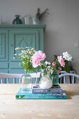 Fresh garden flowers in three small vases and books on table