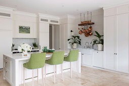 White center block with green bar stools, fitted wardrobes and copper pots in an open kitchen