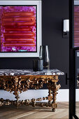Artwork on black wall and antique console with marble top