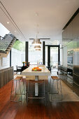 Stainless steel cabinets and island counter in fitted kitchen with dining area in front of terrace doors in background