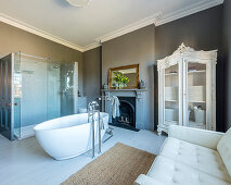 Sofa, oval bathtub and open fireplace in comfortable bathroom