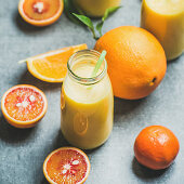 Healthy yellow smoothie with citrus fruit and ginger in bottle over grey concrete background