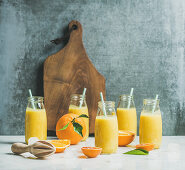 Healthy yellow smoothie with citrus fruit, ginger, ice in bottles on light marble table