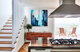 View past island counter with gas hob to sideboard between staircase and balcony