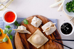 Various raw dumplings on a wooden board next to two sauces (seen from above)