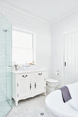 Waschtischmöbel mit Aufsatzbecken vor Fenster, Toilette und frei stehende Badewanne in weißem Badezimmer