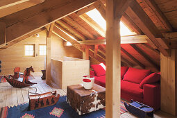 Red sofa, cowhide pouffe and rocking horse in wood-panelled attic room