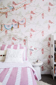 Bett mit weiß-rosa gestreifter Bettwäsche und Tapete mit Vogelmotiv im Mädchenzimmer