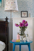 Glasvase mit pinkfarbenen Dahlien auf blauem Nachttisch neben Stehlampe