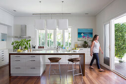 Kitchen island and bar stool in open kitchen with terrace access, woman in the background