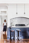 Counter with bar stools in open kitchen, woman in background