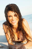 A brunette woman wearing a pastel pink bikini lying in the sea