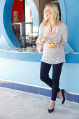 A blonde woman wearing a knitted jumper and dark trousers holding a fruit salad