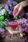 Lilac flowers being sprinkled into homemade lilac syrup