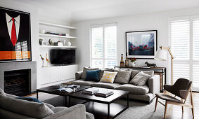 Sofas, a chair and a coffee table in front of a fireplace, vintage posters on a mantelpiece, white shelves and TV furniture in the background