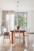 Dining table with white chairs and bench in front of French windows