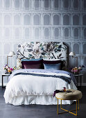 Bed with a floral headboard in front of a wallpaper with an architectural motif