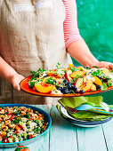 Frau serviert Sommersalat mit Pfirsichen und Blaubeeren