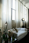 White sofa against brick wall with industrial windows and long curtains