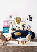 Blonde Frau sitzt auf blauem Sofa, gerahmte Kunstwerke an der Wand