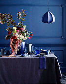 Laid table in shades of blue with a lush bouquet of flowers, pendant lights above