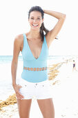 Brünette Frau in hellblauem Badeanzug und weißen Shorts am Strand
