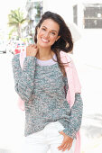 A brunette woman wearing a grey flecked jumper with a pink jumper over her shoulders