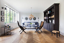 Dark bookcase, chairs, coffee table and sofa in living room with herringbone parquet floor