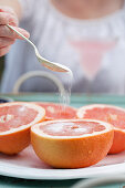 A woman sprinkling sugar onto a platter of grapefruit halves