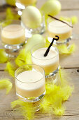 Vanilla eggnog in glasses for Easter, decorated with yellow feathers and Easter eggs