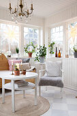 Runder Tisch, Armlehnstuhl, Holzbank und Zimmerpflanzen in skandinavischem Wintergarten