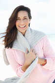 A brunette woman wearing a pink jumper with a grey jumper over her shoulders