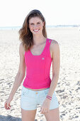 A young woman on a beach wearing a pink top and light shorts
