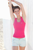 A young woman on a beach wearing a pink top and light shorts