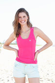 A young woman on a beach wearing a pink top and light shorts