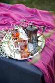 Tea glasses and silver teapot on tray with leafy twigs