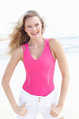 A blonde woman on a beach wearing a pink top and light shorts